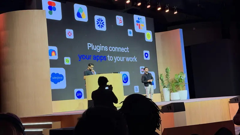 Two presenters under a slide reading Plugins connect your apps to your work, with Salesforce, Slack, Figma and Zoom logos